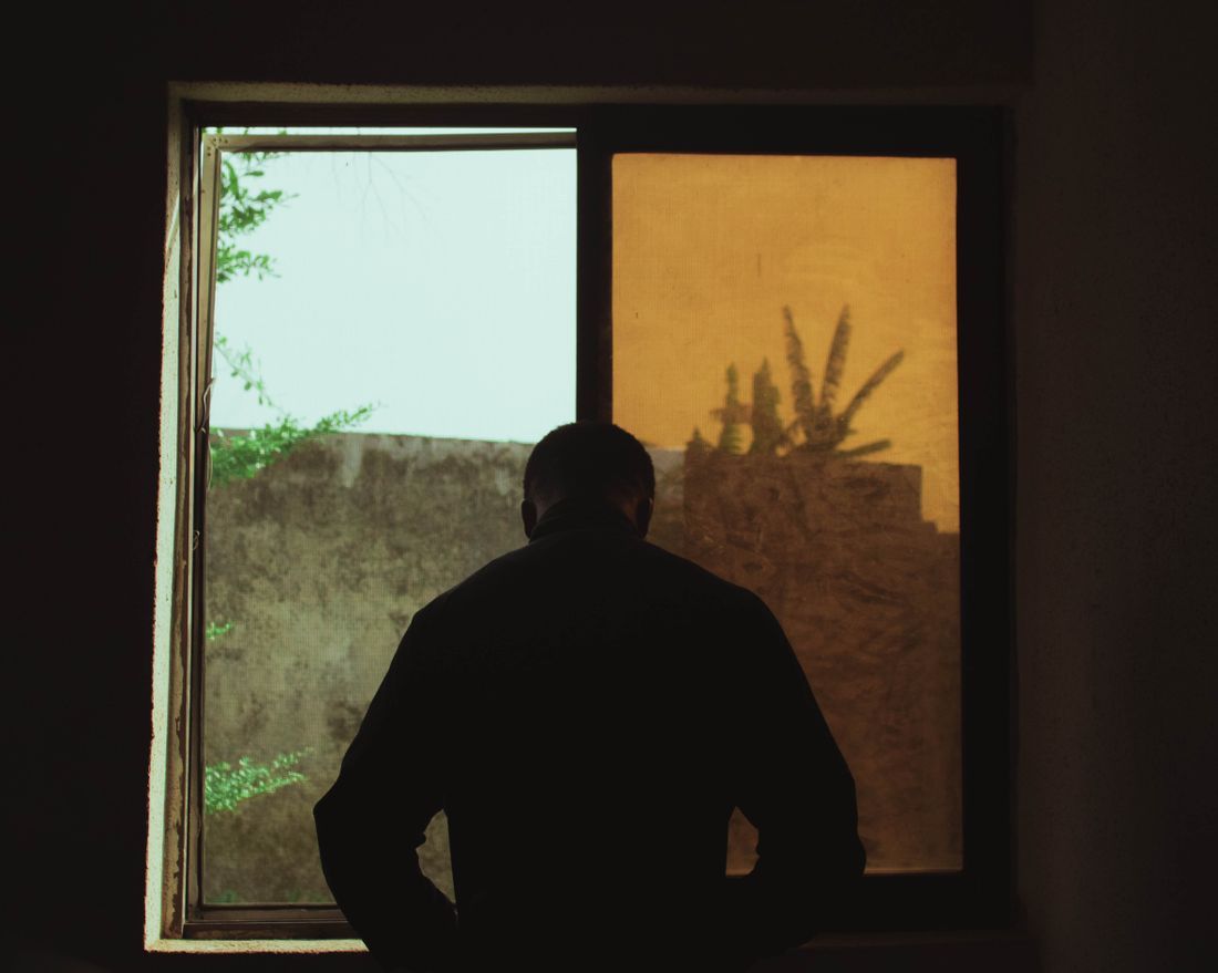 A man standing at a window with his back to the room
