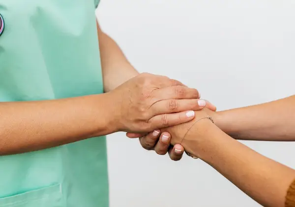 A caregiver gently holding a patient's hands in both of hers