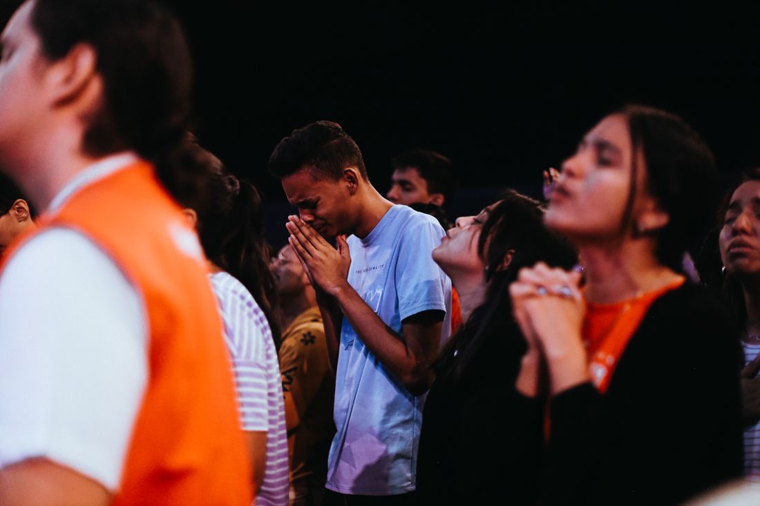 A young man in tears praying among other youth
