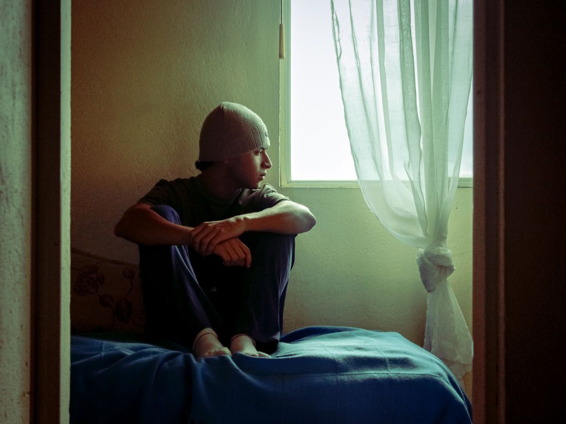 A teen sitting alone by a window, lost in thought