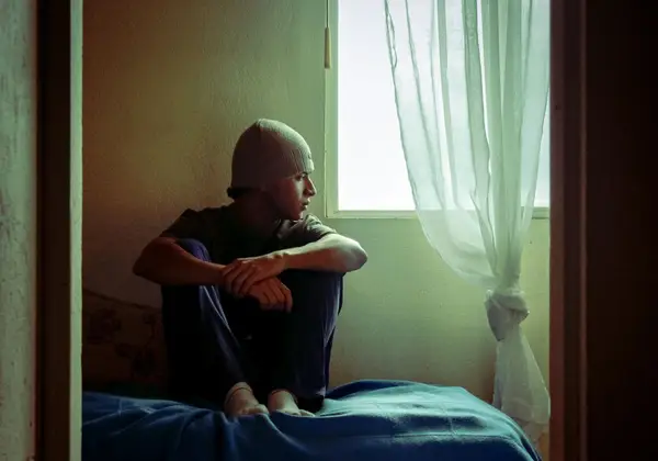 A teen sitting alone by a window, lost in thought