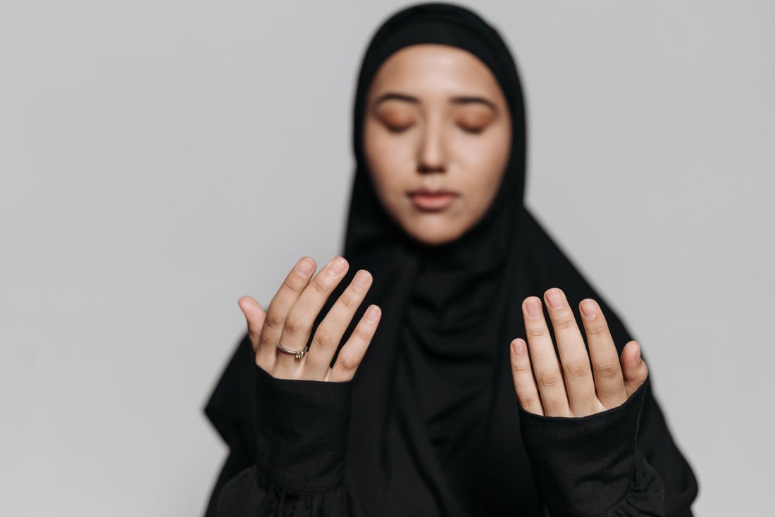 A woman in hijab with hands open in prayer