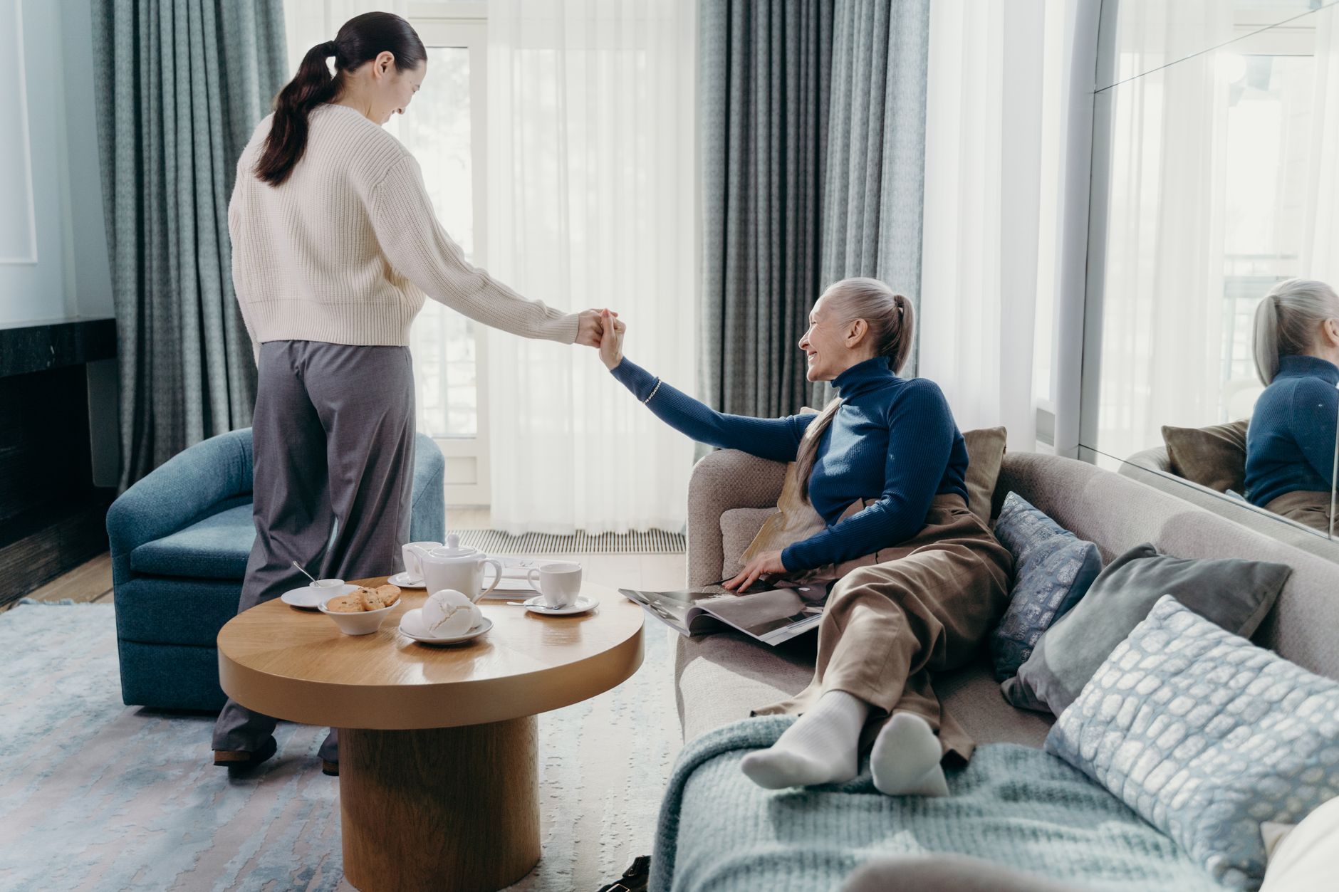 A caregiver gently helping an older woman up from the sofa