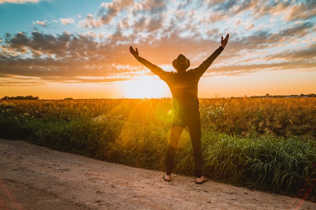 A person lifting their arms toward the sunrise in an open field
