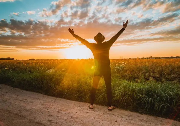 A person lifting their arms toward the sunrise in an open field