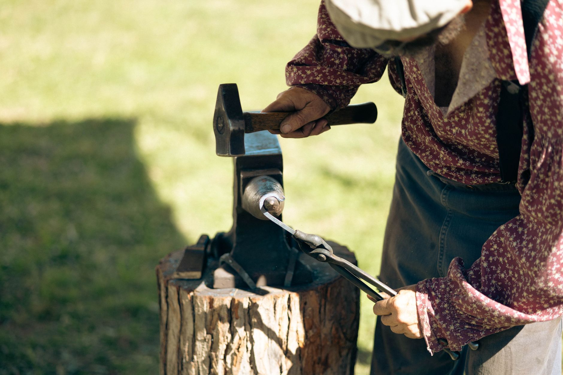 A craftsman's hands shaping hot metal at an anvil in the sun