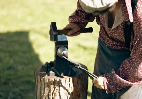 A craftsman's hands shaping hot metal at an anvil in the sun