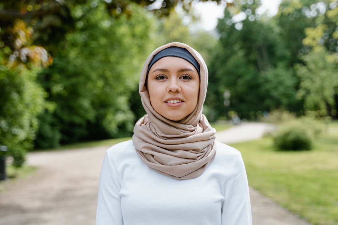 A woman in a hijab with a gentle smile in a green park