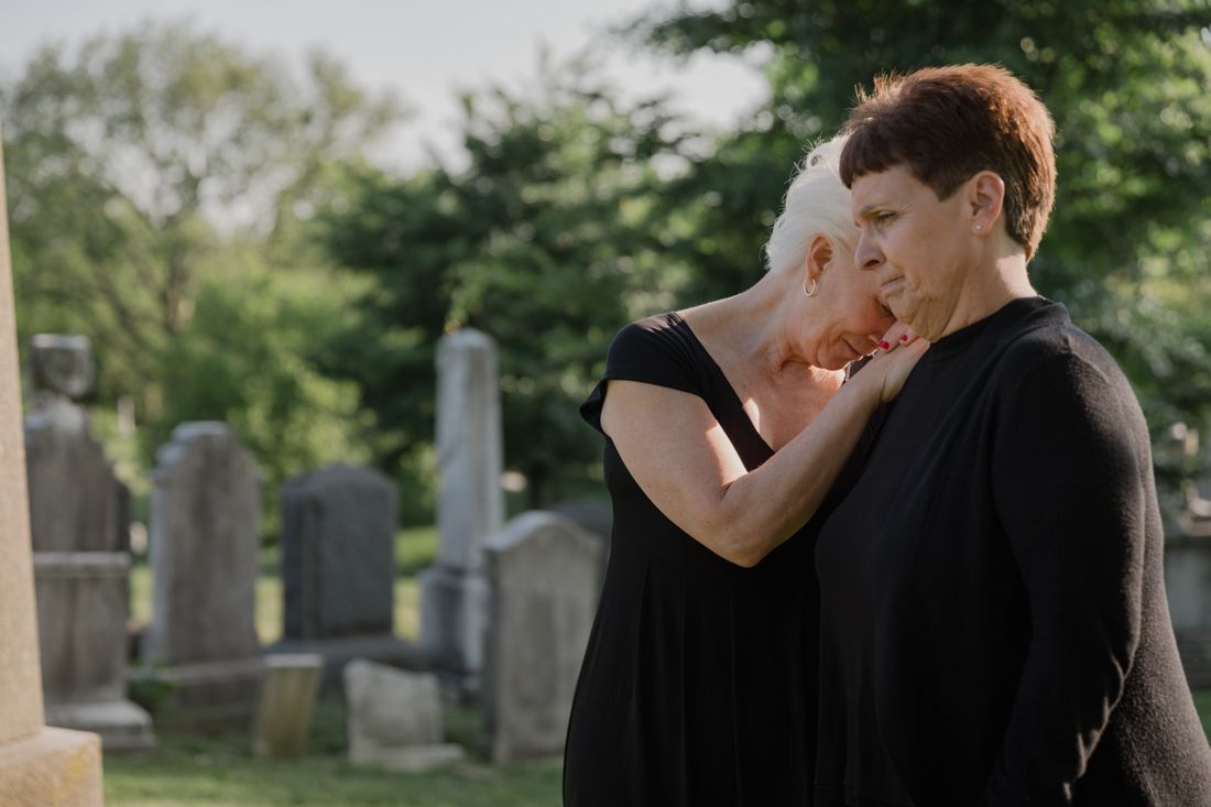 Two women comforting one another at a graveside