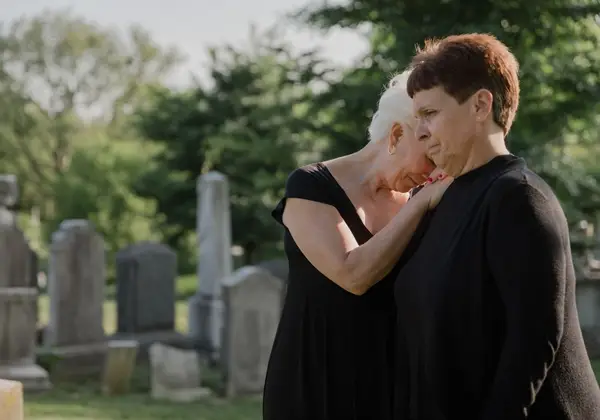 Two women comforting one another at a graveside