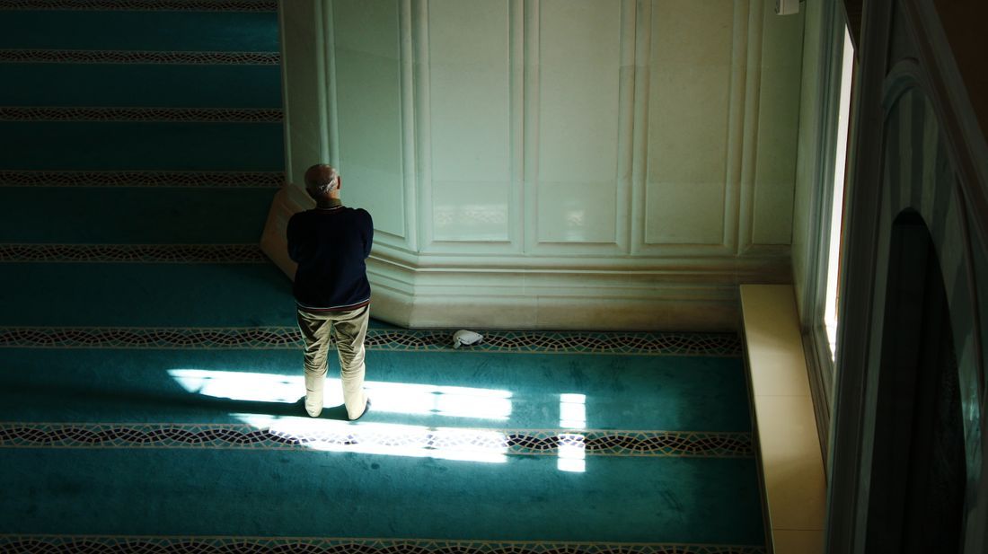 A man praying alone in the light of a mosque