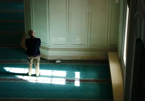 A man praying alone in the light of a mosque