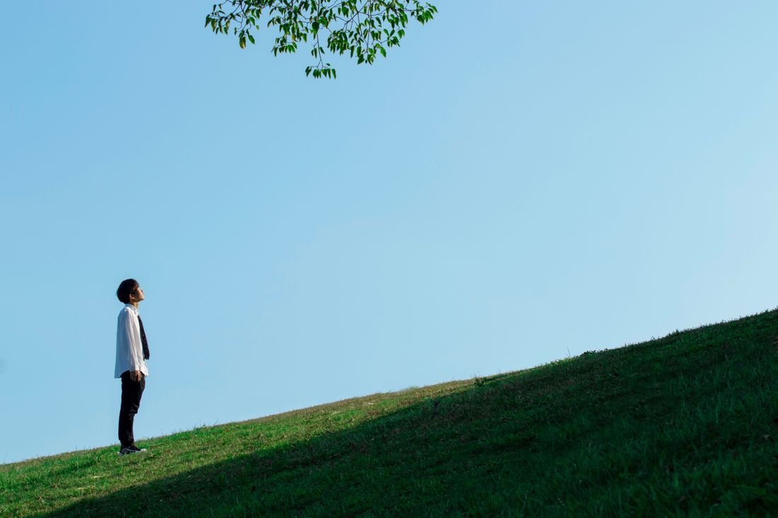 A man standing on a hillside, looking up at an open sky