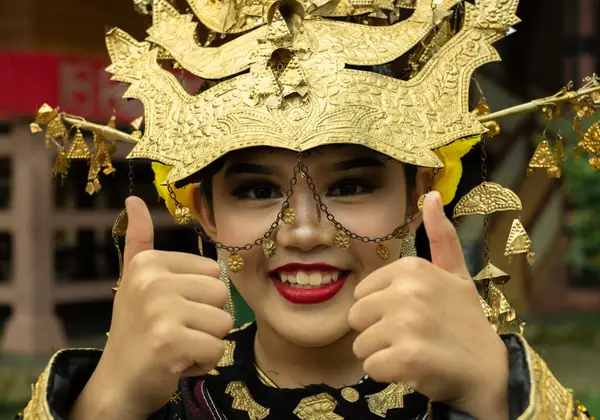 A smiling young Indonesian woman in golden ceremonial dress