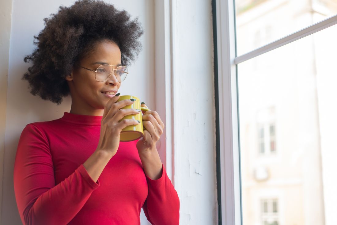 A woman quietly holding a mug by a window in the morning light