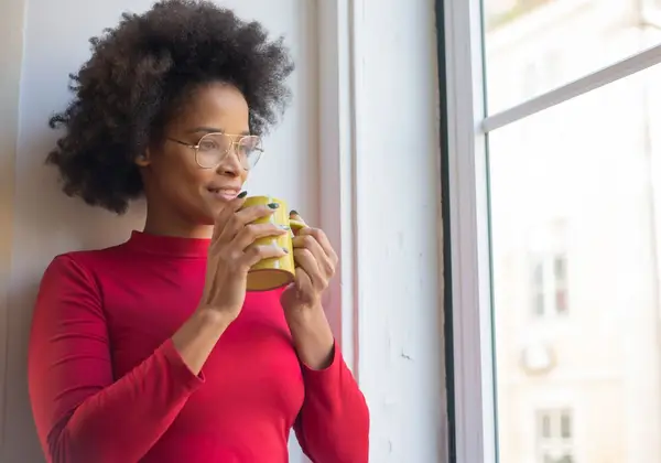 A woman quietly holding a mug by a window in the morning light