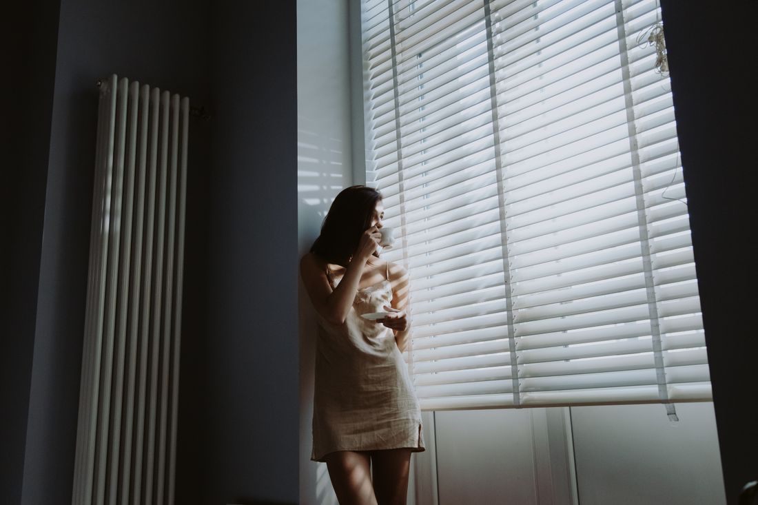A woman standing alone with coffee in the quiet of a sunlit room