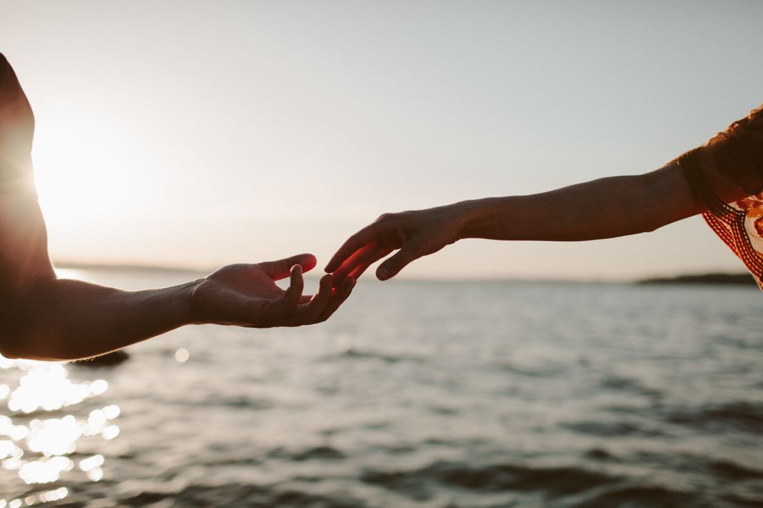 Two hands reaching for one another over the water at sunset