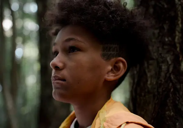 Close-up of a teenage boy looking up, hopeful, in the woods
