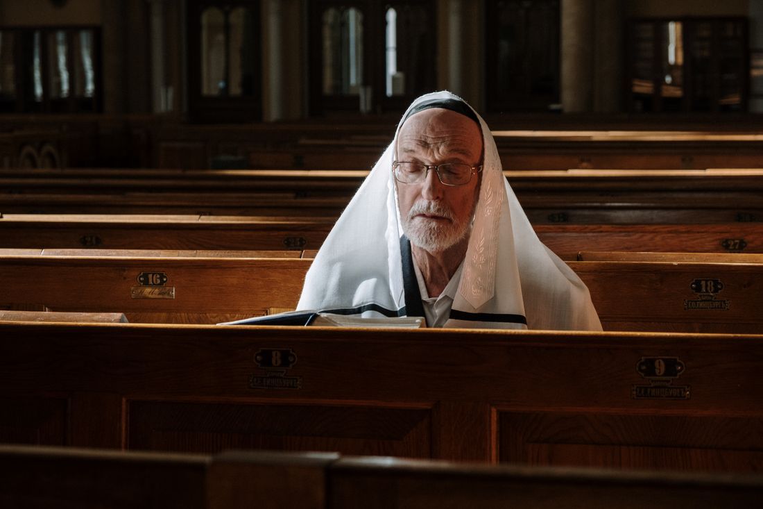 An older man in a tallit praying with eyes closed