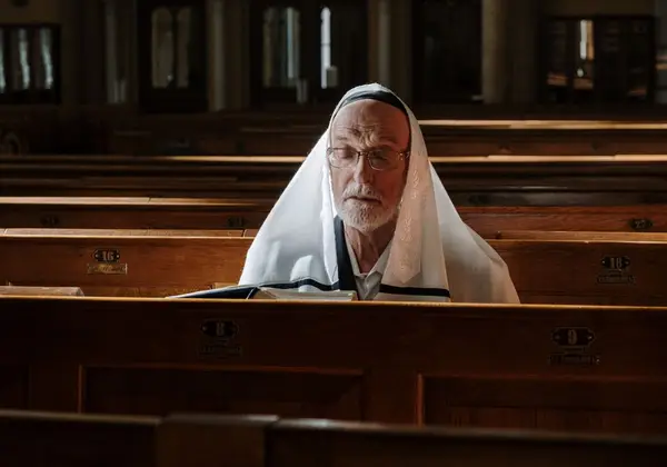 An older man in a tallit praying with eyes closed