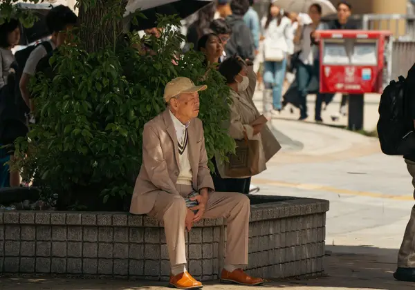 An elderly Japanese man resting on a city street