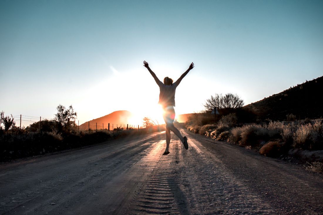 A person leaping for joy on an open road at dawn