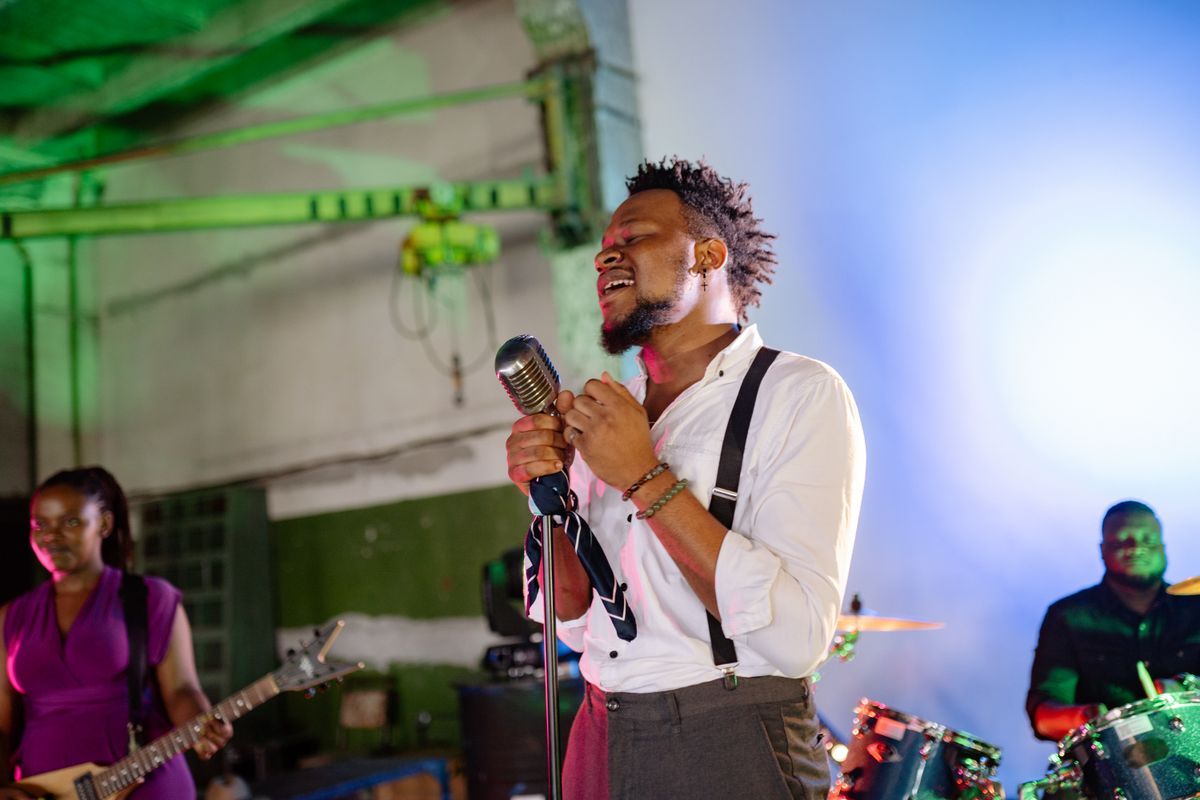 A man singing passionately at a vintage microphone with a band behind him