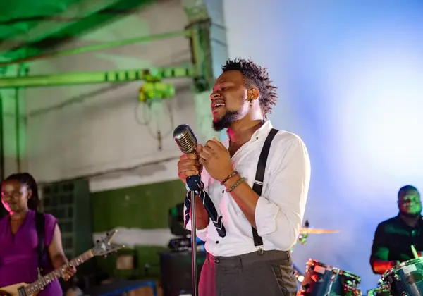 A man singing passionately at a vintage microphone with a band behind him