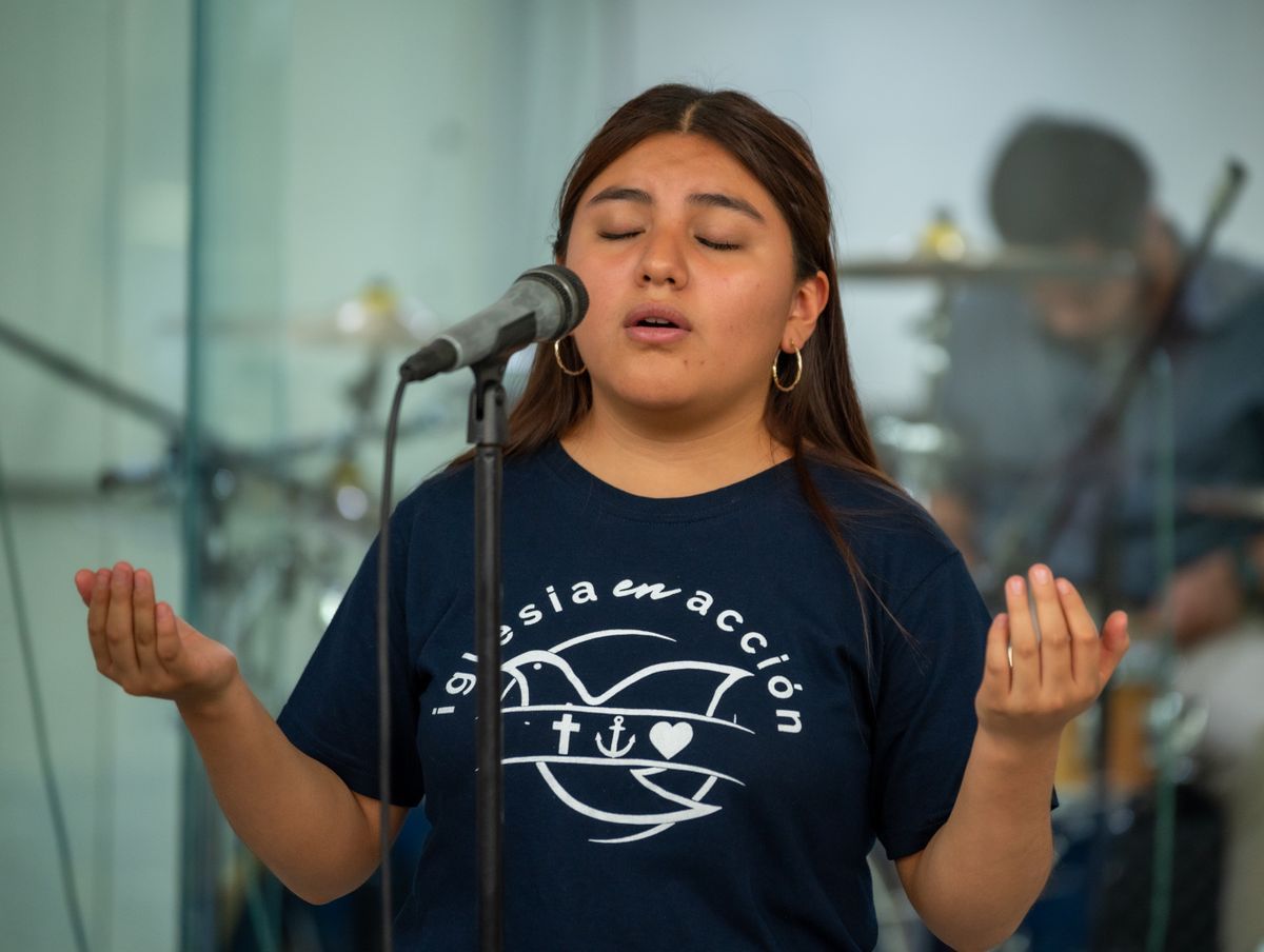 A young woman singing with eyes closed at a microphone during a church service