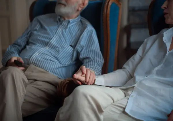 An older couple holding hands, their wedding rings visible