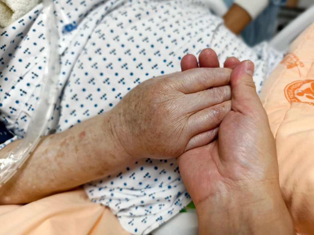 A loved one holding a patient's hand at the hospital bedside