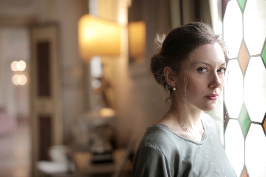 A woman standing thoughtfully by a stained-glass window