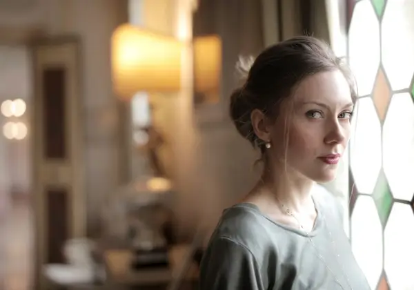 A woman standing thoughtfully by a stained-glass window