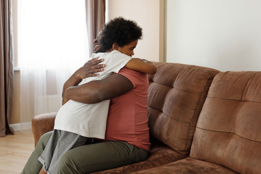 A father embracing his teenage son on the couch