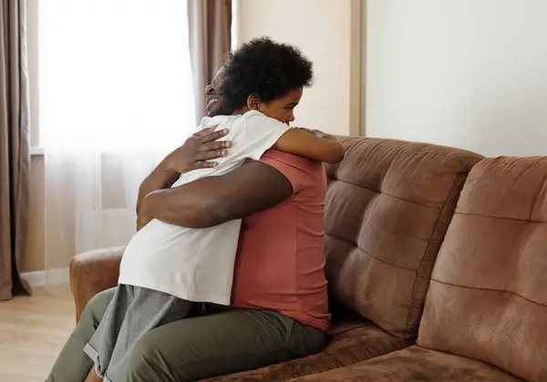 A father embracing his teenage son on the couch