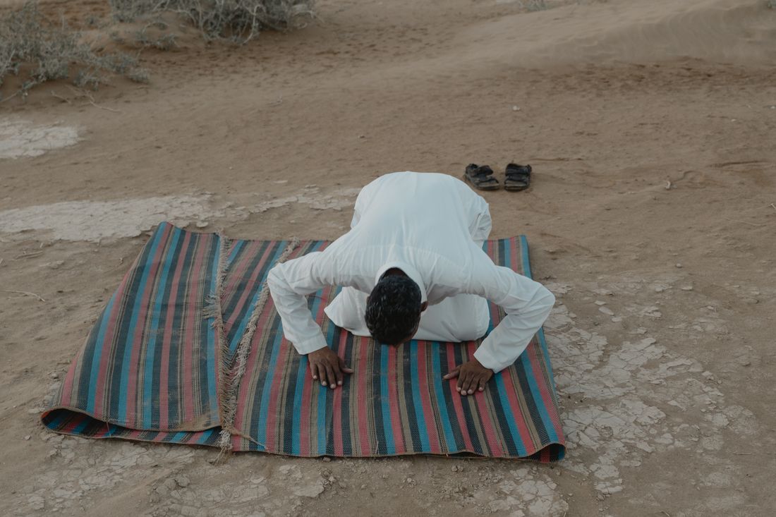 A man in prayer, bowing low on a mat in the open air