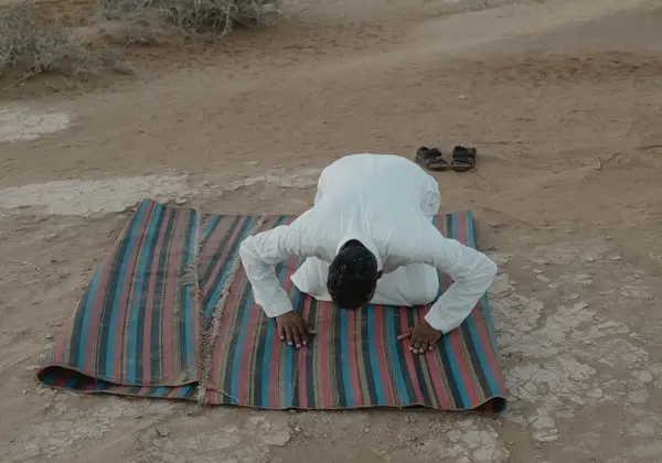 A man in prayer, bowing low on a mat in the open air