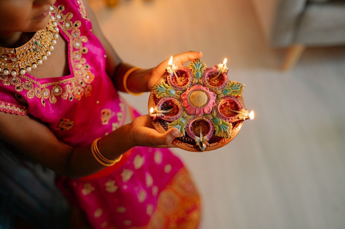 A woman in festive dress holding a plate of lit diyas