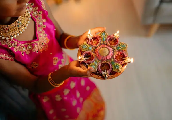 A woman in festive dress holding a plate of lit diyas