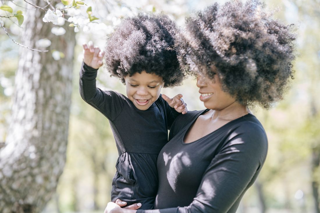 A mother and her young daughter laughing together outdoors