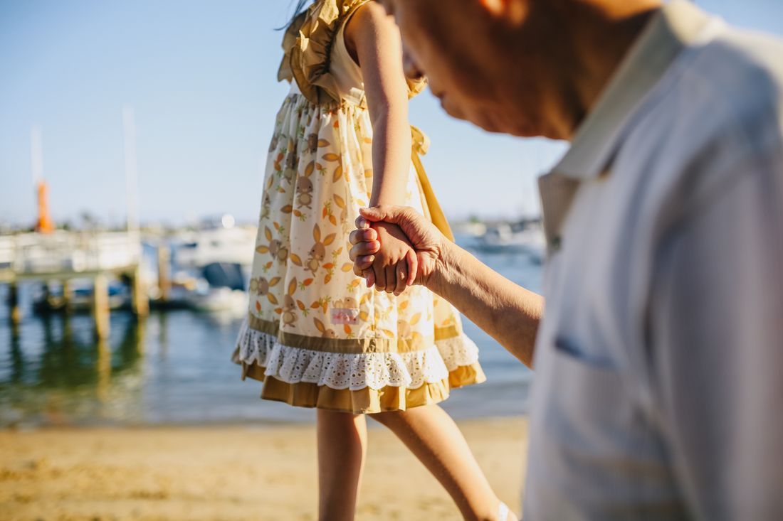 A grandfather holding his granddaughter's hand by the water