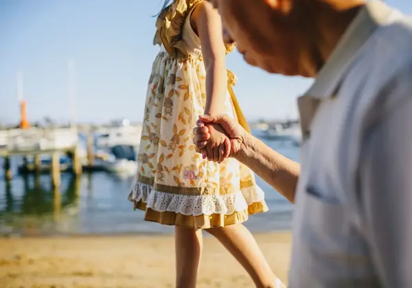 A grandfather holding his granddaughter's hand by the water