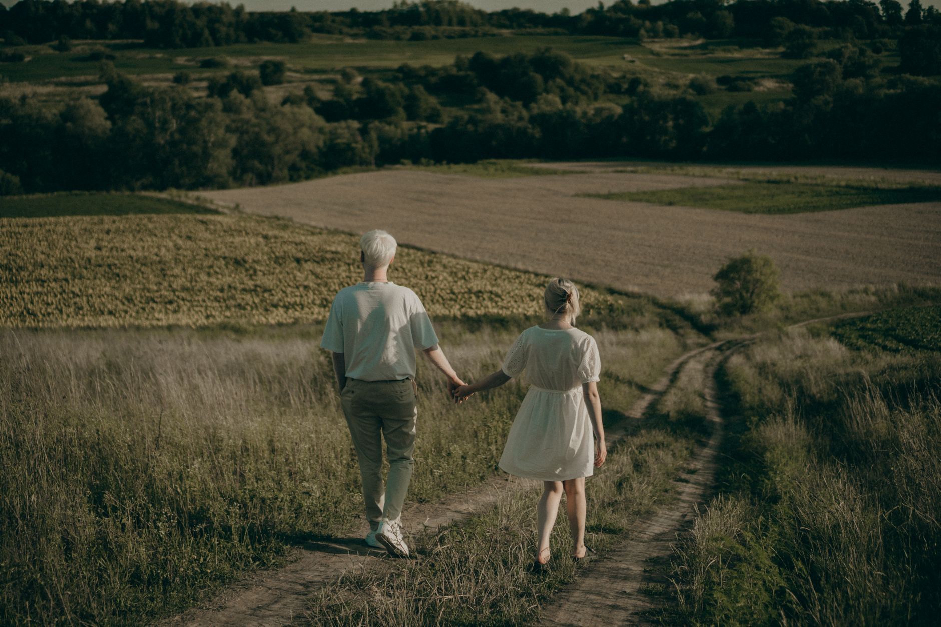 A couple walking hand in hand along a country path at golden hour