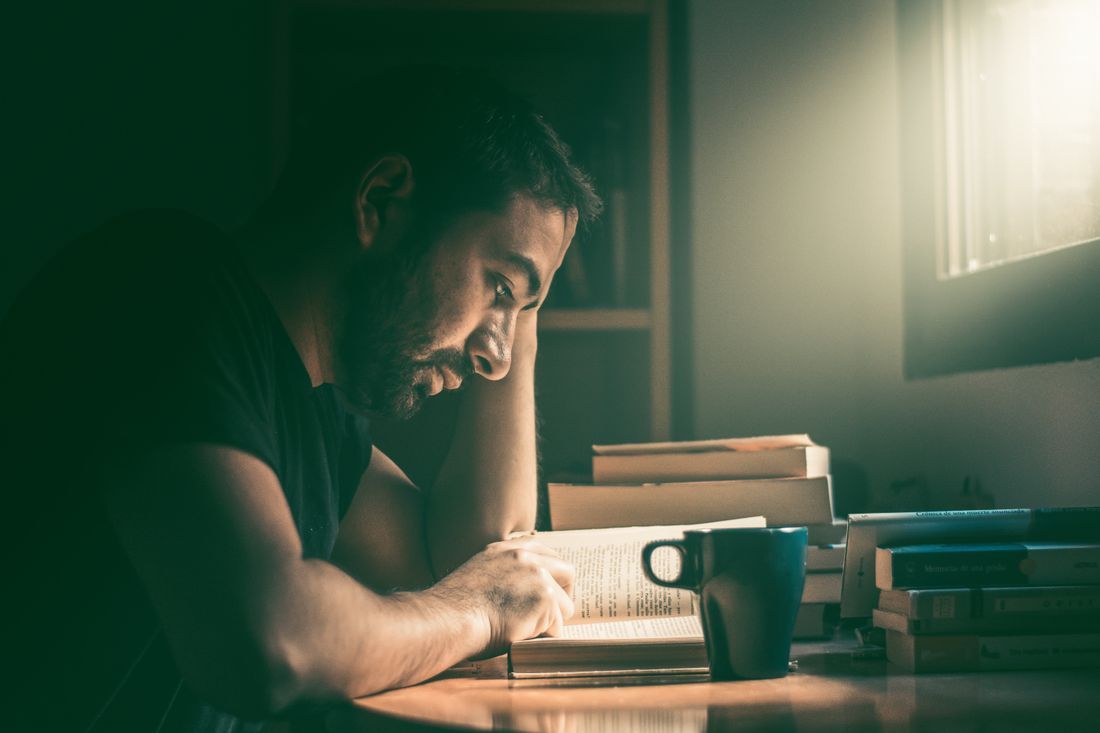 A man reading at a desk by warm lamplight