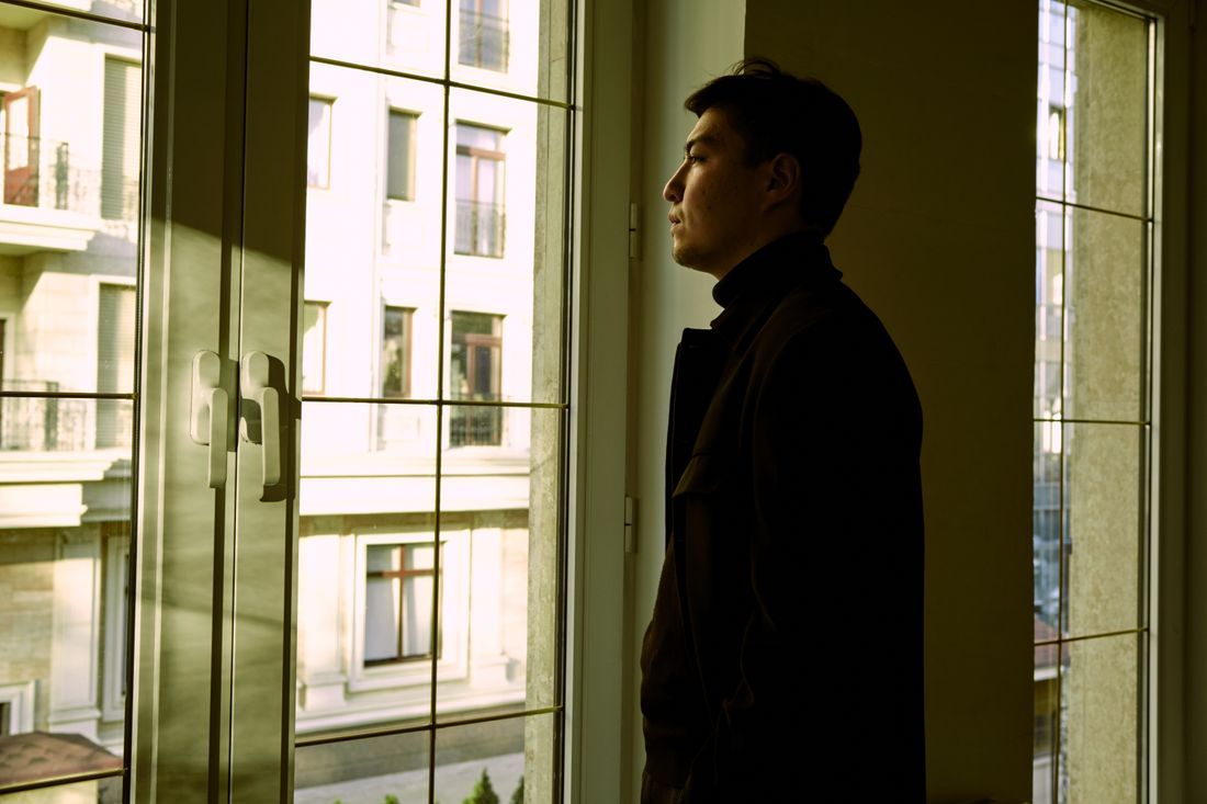 A young man looking out a window in thought
