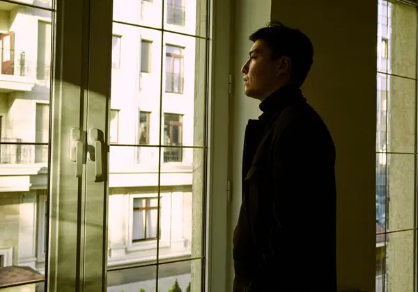 A young man looking out a window in thought