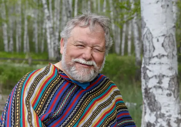 A cheerful elderly Russian man among birch trees