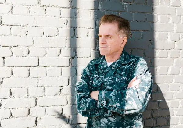 A Navy veteran leaning against a wall, lost in thought