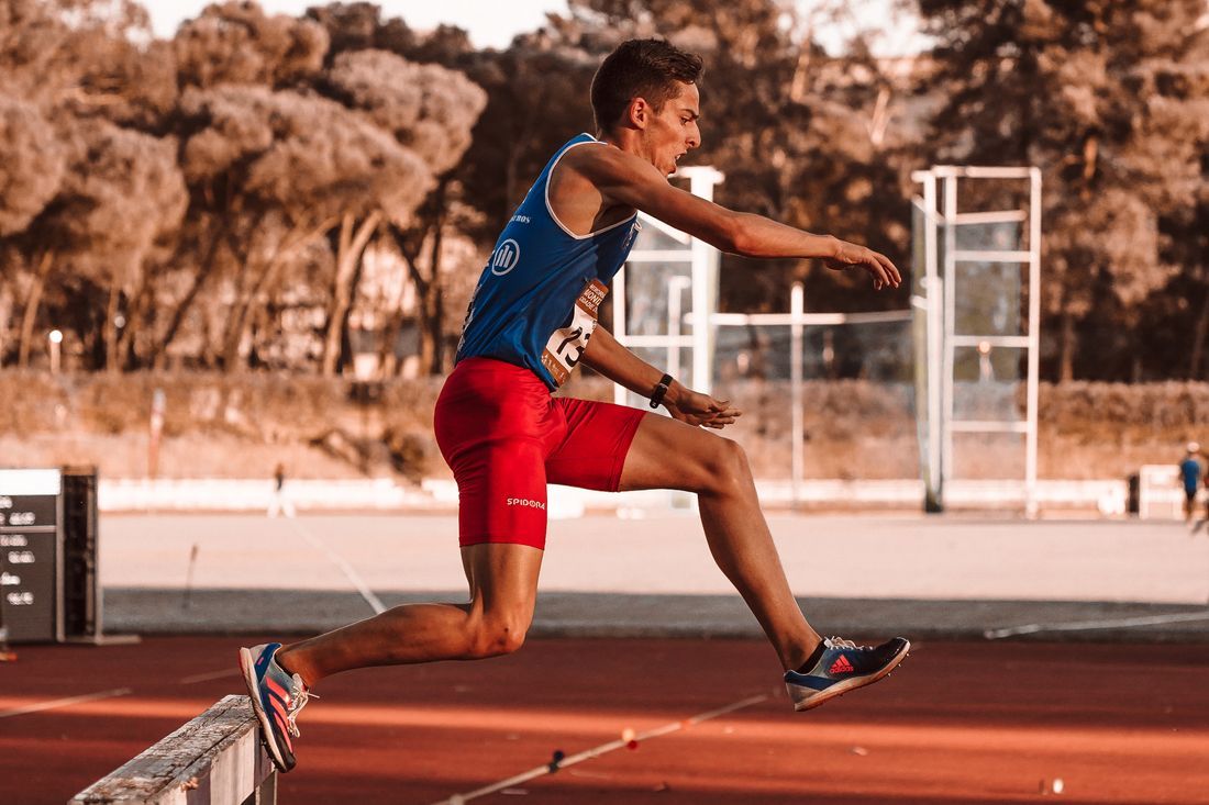 A track athlete clearing a hurdle in full stride